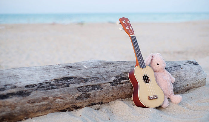 A toy guitar and a stuffed animal sit on the beach, showcasing playful musical toys for babies in a sunny setting.
